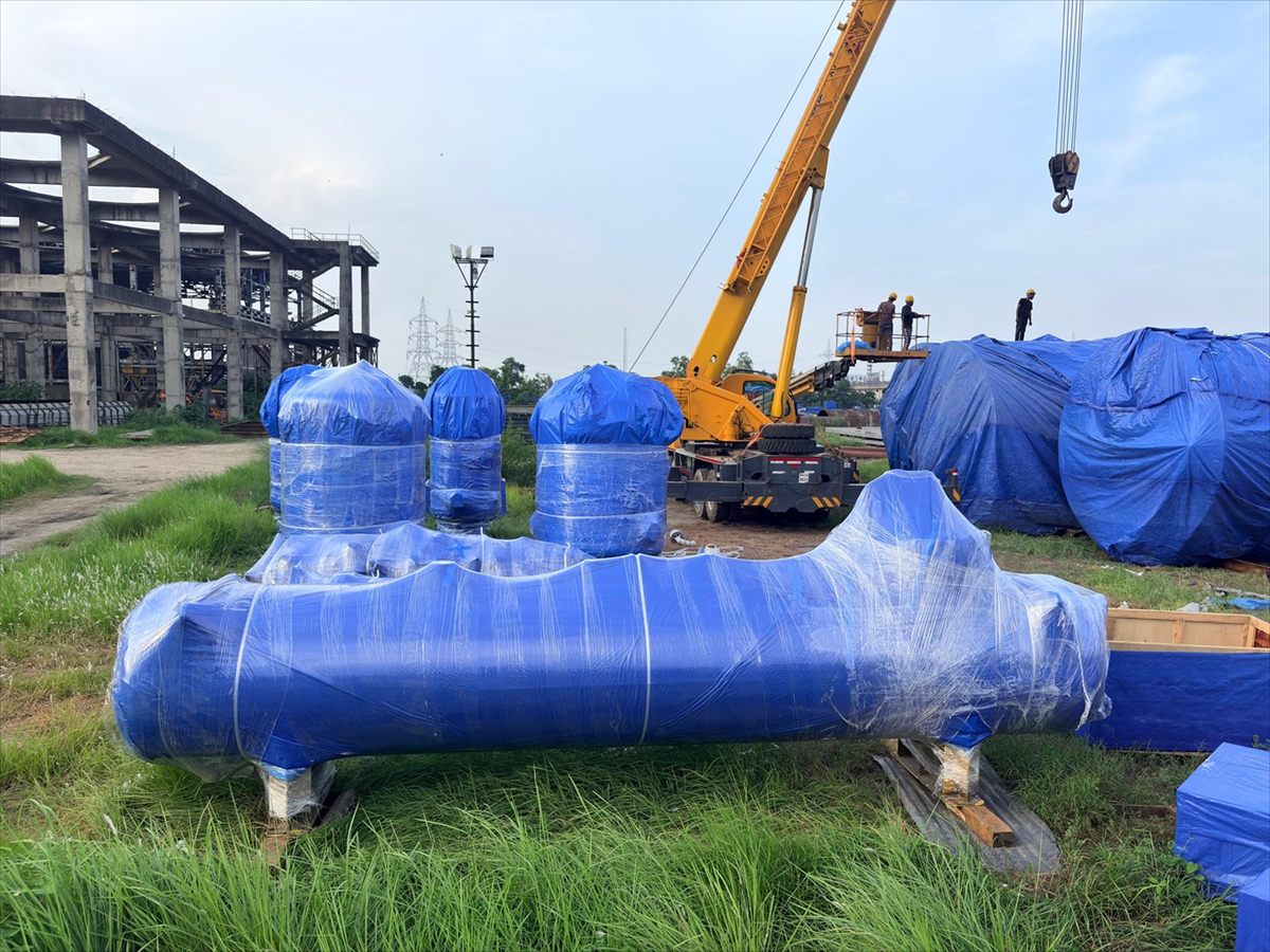 Fabricated manifold header wrapped in place at a project site with crane standing by