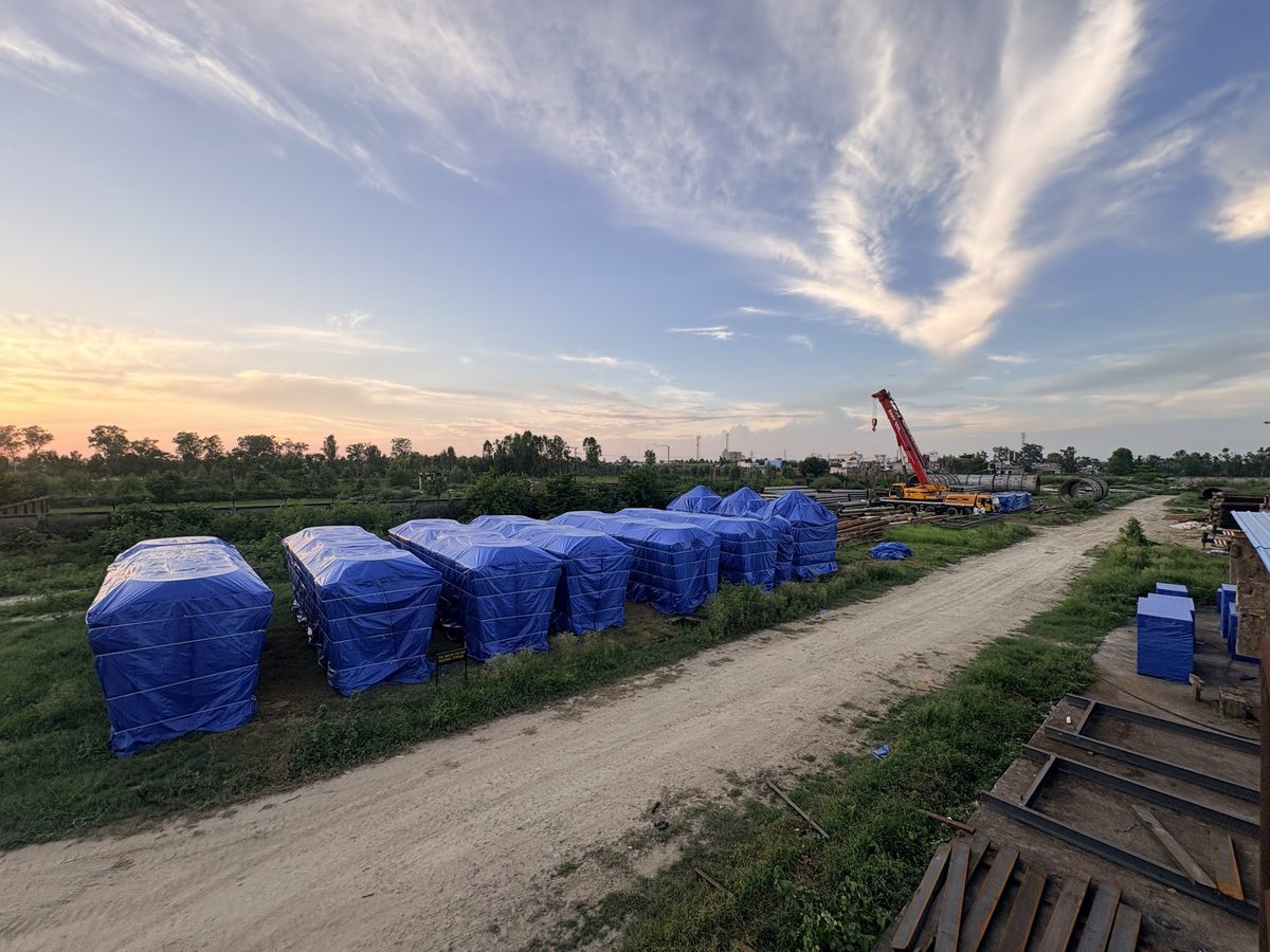 Row of oversized equipment units in blue industrial PE covers staged in a yard before shipping