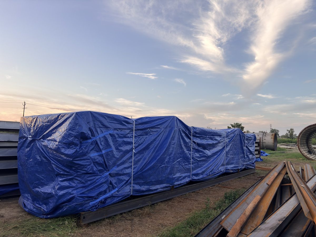 Oversized industrial load fully enclosed in a blue form-fit polyethylene 3D cover on a steel skid